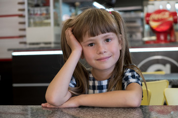 Child girl sitting in fast food restaurant behind empty table waiting for food.