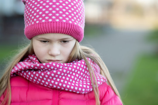 Sad child girl in warm knitted winter clothes outdoors.