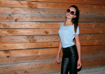 Modern girl with ponytail, makeup, wearing black leather shirt and pants, sunglasses, posing near wooden wall, walking is the night on the street.