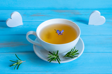 Cup of rosemary tea and decorative white hearts on blue wooden background.