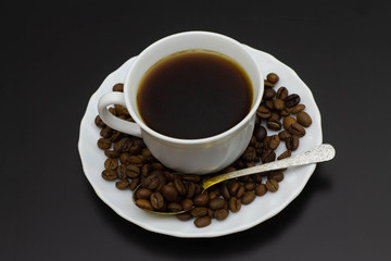 cup of coffee on a plate with grains and a spoon on a dark background