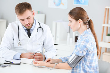 Fototapeta premium Male doctor measuring blood pressure of female patient in clinic