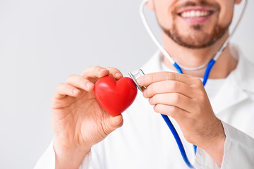 Male cardiologist with red heart on light background, closeup
