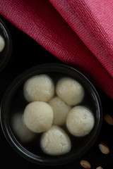 Mouth watering white rasgullas kept in a black bowl. 	