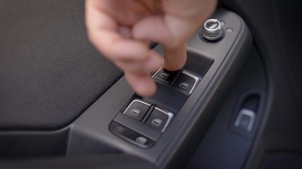 driver is pressing buttons of window switches with remote control inside modern car, closeup view of hand