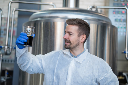 Technologist looking through glass of beverage product and testing quality. - Powered by Adobe