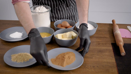 The man is a cook in an apron, his hands in gloves. On the table are the ingredients for the cupcake. The dough will be prepared, the spicy part.