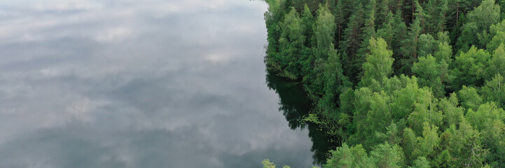 Topview of wood and riverside. Horizon dividing cloudy sky and green wild nature. Landscape of valley with trees and water with reflection on summer time