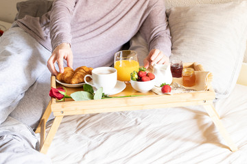 Obraz na płótnie Canvas Woman eat breakfast in the bed inside a bedroom. Wooden try with coffee, orange juice, croissant, jam ,strawberry and red rose flower