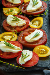 Slices of yellow and red tomatoes with mozzarella and herbs. Italian Caprese salad on a slate slab