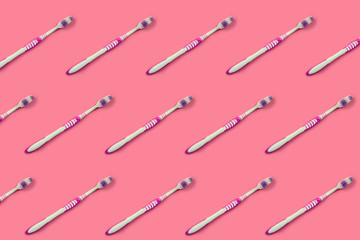A lot of toothbrushes lie on a pastel pink background