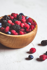 Juicy fresh blueberries, raspberries and blackberries in a white plate on old wooden background