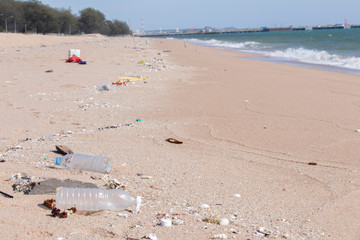 The plastic bottle rubbish on the sand at the beach, with sea water and industrial bridges far away It's a marine environmental problem.