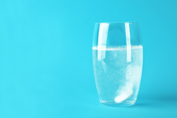 Glass of water with effervescent tablet on light blue background, space for text