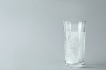 Glass of water with effervescent tablet on light grey background, space for text