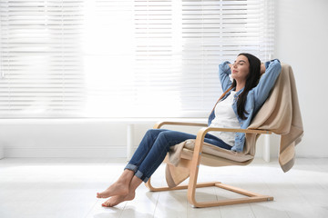 Young woman relaxing in armchair near window at home