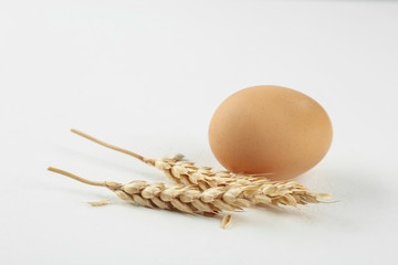 Raw chicken egg and wheat spikes on white table