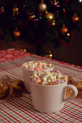 Obraz na płótnie Canvas White mugs of hot chocolate beverage with colorful marshmallow and star shaped gingerbread cookies on Christmas tree background 