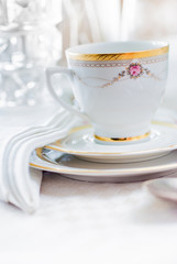 Vintage tea or coffee cup with gold rim on saucer. White linen tablecloth and napkin. With space for copy.