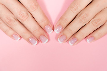 Top view flatlay closeup photography of two female hands with beautiful classic french pink and white manicure. Fingers isolated on pastel pink background. Horizontal color image.