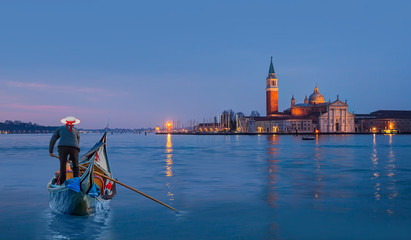 Venetian gondolier punting gondola through grand canal waters - View of San Giorgio Island in Venice with wooden buoys in Giudecca Canal "Elements of this image furnished by NASA" © muratart