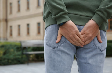 Man suffering from hemorrhoid pain outdoors, back view