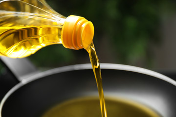Pouring cooking oil from bottle into frying pan, closeup