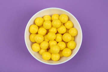 Delicious lemon drops on purple background, top view