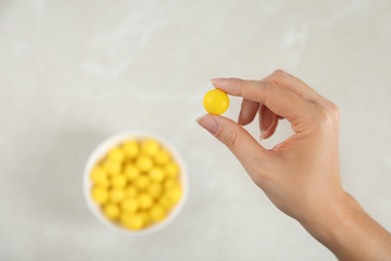 Woman holding tasty lemon drop above light table, top view