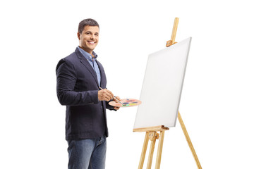 Young man painting on a canvas and smiling at the camera