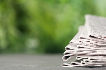 Stack of newspapers on grey table against blurred green background, space for text. Journalist's work