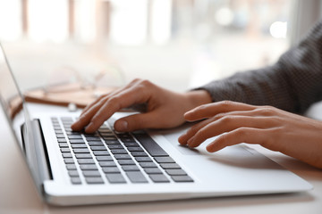 Young blogger working with laptop at table indoors, closeup