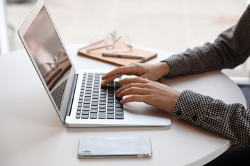 Young blogger working with laptop at table indoors, closeup