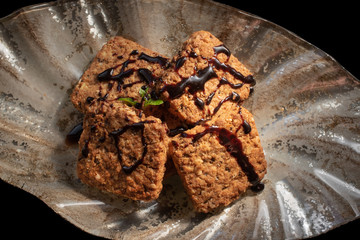 Integrated cookie is in gilded plate decorated with chocolate syrup and mint, isolated on black background, top view