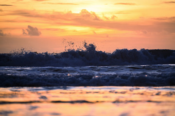 Fototapeta na wymiar (Selective focus) Stunning view of waves crashing on a beautiful beach during a dramatic and romantic sunset. Lombok Island, West Nusa Tenggara, Indonesia.