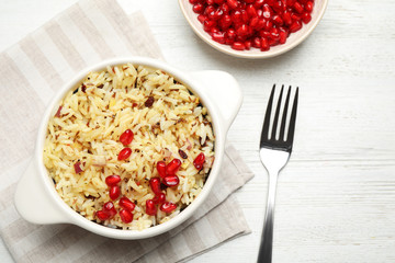 Tasty rice pilaf with pomegranate grains served on white wooden table, flat lay