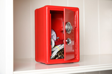 Open red steel safe with money and jewelry on shelf