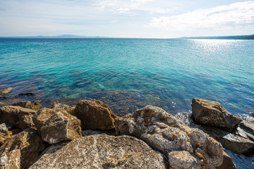 Fototapeta na wymiar Beautiful sunny summer landscape of blue peaceful sea water, clear sky and big stones in foreground of image. Picturesque Greece nature, Chalkidiki. Horizontal color photography.