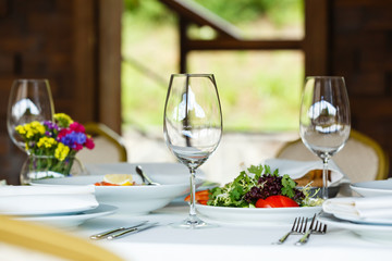Restaurant table served for two persons. Wine glasses, plates, silverware, cutlery. European food, vegan organic salad. Banquet snacks