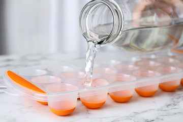 Pouring water into ice cube tray on white marble table, closeup