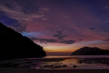 view seaside evening of many rocks on sand beach with mountains and purple sky background, sunset at Khao Chong Kad Bay, Surin island, Phang Nga, south of Thailand.