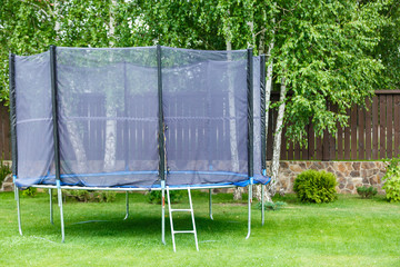 Big trampoline for children and adults. Trampoline with safety net set on green grass beside wooden...