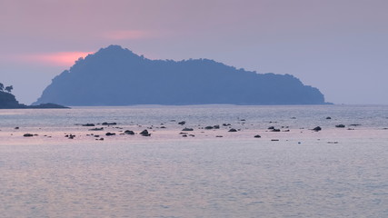 view of many small rocks in the sea with mountain and purple sky in background, sunset at Khao Chong Kad, Surin island, Mu Ko Surin National Park, Phang Nga, southern of Thailand.