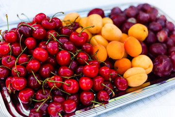 Fruit platter. Red, orange, purple fruit on a white plate. Assortment of fruit. Cherry, plu, peach, apricot, nectarine. White background