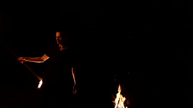Young man in the dark depicts rotating burning torch. Fire show