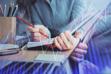 A woman hands writing information about stock market in notepad. Forex chart holograms in front....