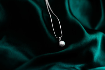 Luxury white gold pearl necklace on dark emerald green silk background, holiday glamour jewelery...