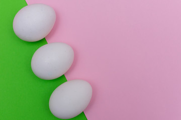 Three Easter holiday flat lay with white egg on a solid bright green, and light pink pastel background with copy space.