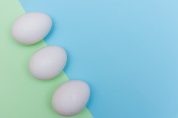 Three Easter holiday flat lay with white egg on a solid light green and blue pastel background with copy space.