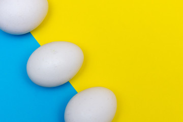 Three Easter holiday flat lay with white egg on a solid bright blue and yellow vibrant background with copy space.